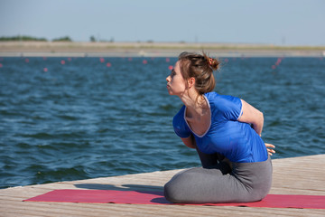 Fototapeta premium Young woman doing yoga in morning park near lake
