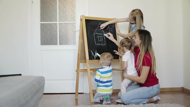 Mother with children draw chalk on a blackboard.