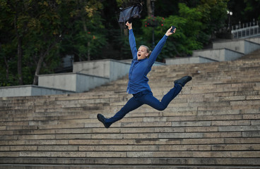 Happy businessman jumping with cityscape background. The best day. Young  man in formal wear...