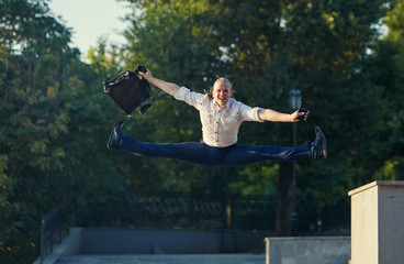 Happy businessman jumping with cityscape background. The best day. Young  man in formal wear...