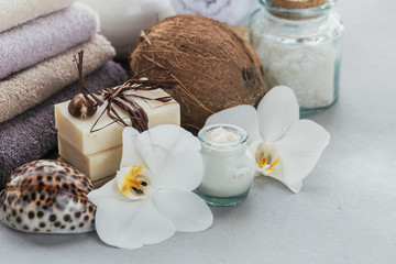 Organic cosmetics with coconut oil, sea salt, towels and handmade soap with white orchid flowers on grey background
