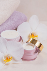 Fototapeta na wymiar Bottles of hand or face cream or facial mask, towels and white orchid flowers on light background.