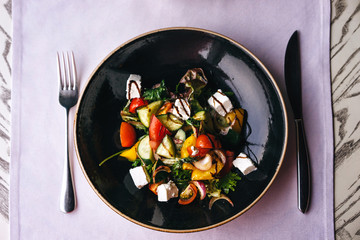 Appetizing dish in the restaurant, serving on the table with a lilac tablecloth. Greek salad of tomato, cheese, pepper, greens, seasoned with balsamic vinegar. Top view meal. Vegetarian dinner