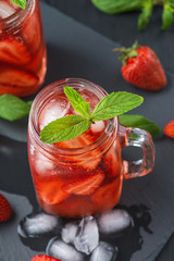 Fresh strawberry smoothie. Fresh summer cocktail with strawberries and ice cubes on a dark background on a black wooden table.