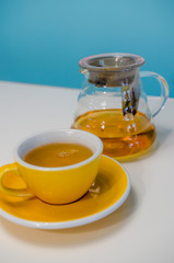 Yellow cup of tea and glass teapot on the table. Blue background