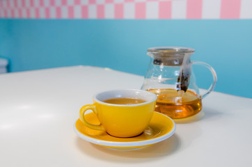 Yellow cup of tea and glass teapot on the table. Blue background