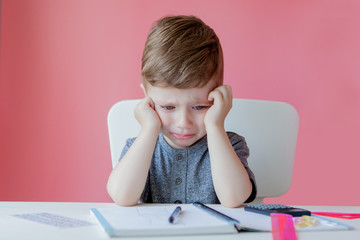 Portrait of cute kid boy at home making homework. Little concentrated child writing with colorful pencil, indoors. Elementary school and education. Kid learning writing letters and numbers