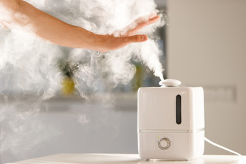 man holds hand over steam aroma oil diffuser on the table at home, steam from the air humidifier, free space. Ultrasonic technology, increase in air humidity indoors, comfortable living conditions - obrazy, fototapety, plakaty