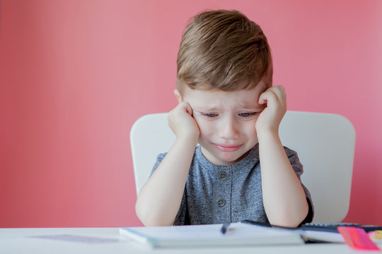 Portrait of cute kid boy at home making homework. Little concentrated child writing with colorful pencil, indoors. Elementary school and education. Kid learning writing letters and numbers