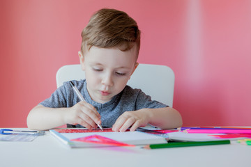 Portrait of cute kid boy at home making homework. Little concentrated child writing with colorful pencil, indoors. Elementary school and education. Kid learning writing letters and numbers