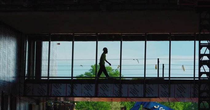 Silhouetted, slow-motion shot of a construction worker crossing a bridge walkway.