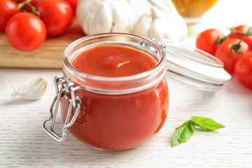 Jar of tasty tomato sauce on wooden table, closeup