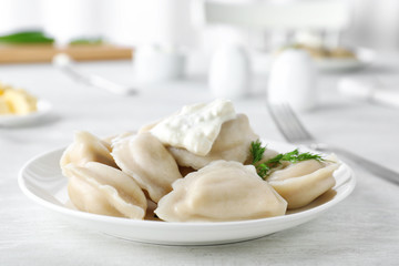 Plate of tasty dumplings served with sour cream and dill on table