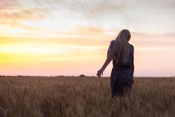 A thin girl in a dress whirls around a wheat field at sunset.