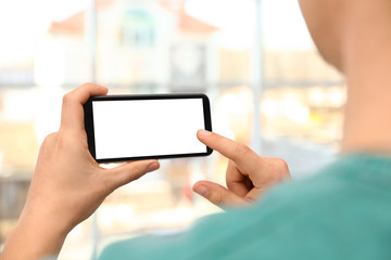 Man holding smartphone with blank screen on blurred background, closeup of hands. Space for text