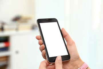 Woman holding smartphone with blank screen indoors, closeup of hands. Space for text