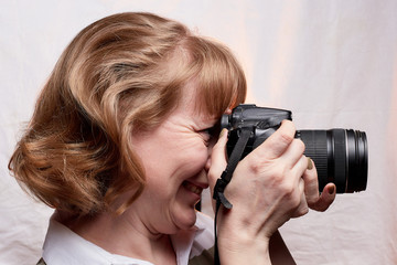 Blonde-haired female photographer with photo camera in her hands on a white background