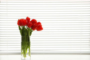 Window with blinds and beautiful bouquet on sill, space for text