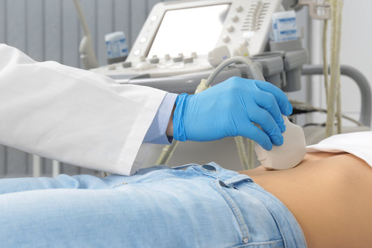 Doctor conducting ultrasound examination of patient's abdomen in clinic, closeup