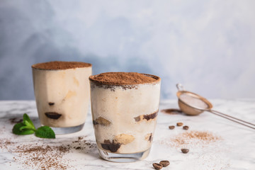 Two glasses of tiramisu cake on table against color background, space for text