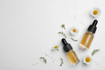 Composition with chamomile flowers and cosmetic bottles of essential oil on white background, top...
