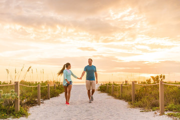 Happy young couple in love walking on romantic beach stroll at sunset. Lovers holding hands on Florida vacation holidays. People walking on summer evening lifestyle. © Maridav