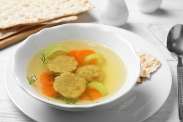 Bowl of Jewish matzoh balls soup on white wooden table
