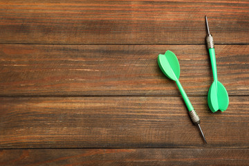 Dart arrows on wooden background, flat lay. Space for text