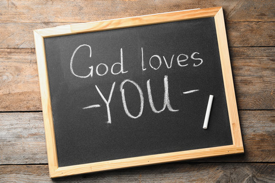 Chalkboard with words GOD LOVES YOU on wooden background, top view