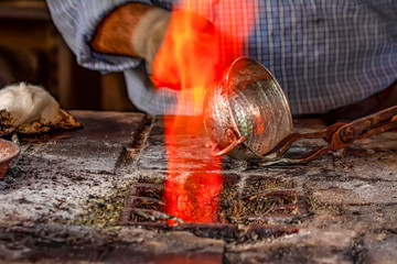 Cropped image of the traditional Turkish tinsmith covering the copper object with tin over fire. 