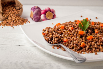 White plate of tasty buckwheat porridge on white wooden table.