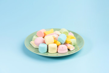 Green plate with marshmallow isolated on blue background.