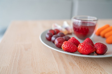 Fruit plate healthy fruits for breakfast on wood table. Strawberries, cranberry juice detox, grapes. Red color food.