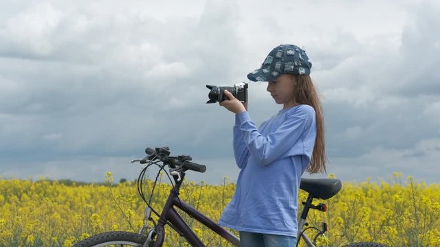 Young photographer. A young girl with a bicycle photographs a flowering field with a camera.