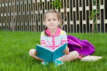 First day of school. child girl schoolgirl elementary school student sitting on the grass near the school and reading a book. Concept back to school. outdoor activities.