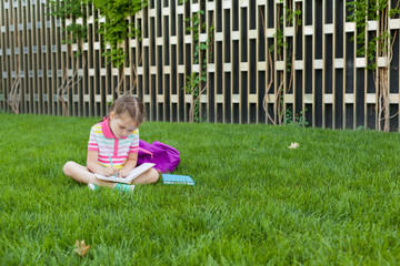 First day of school. child girl schoolgirl elementary school student sitting on the grass near the school and reading a book. Concept back to school. outdoor activities.