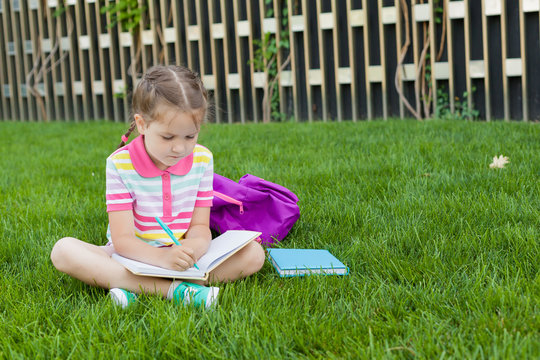 First day of school. child girl schoolgirl elementary school student sitting on the grass near the school and reading a book. Concept back to school. outdoor activities.