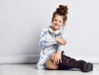 Teen girl kid in fashionable dress, necklace, big black boots and with fashion hairstyle sitting on the floor posing
