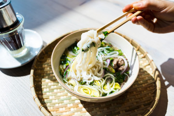 Female Hand With Chopsticks For Asian Food And Fo Bo Soup In White Bowl In Vietnamese Restaurant. Traditional Thai Food.