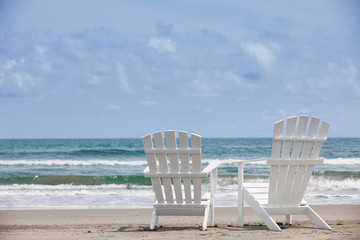 Empty white wooden chairs at a paradisiac beach on the tropics in a beautiful sunny day