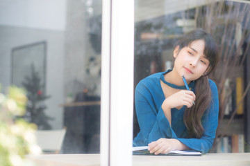 Beautiful young asian woman writer smiling thinking idea and writing on notebook or diary with happy, lifestyle of asian girl is student, female planning working, education and business concept.