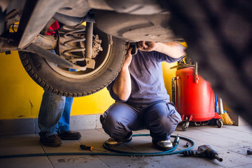 Photo of car mechanics fixing the car. Inside the car shop. - obrazy, fototapety, plakaty