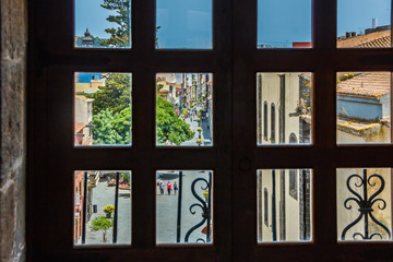 Fototapeta premium View through the window of church tower of the historic town of San Cristobal de La Laguna in Tenerife showing the buildings and streets with mountains in the background