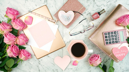 Ultra feminine pink desk workspace with rose gold accessories on white marble background flatlay overhead.