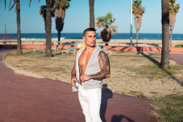 Tattooed bodybuilder sexy male coach at the beach. He poses for the camera and shows his muscles