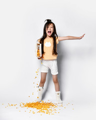 Beautiful asian girl kid at the morning breakfast pouring out corn flakes yawning on gray 