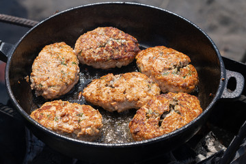 Delicious wild red salmon fish crispy cutlets fried in hot griddle roast on coals, over open fire on campfire. Cooking food on fire during picnic on sunny summer day.