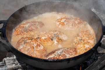 Delicious wild red salmon fish cutlet with gravy fried in hot griddle roast on coals, over open fire on campfire. Cooking food on fire during picnic on sunny summer weather.