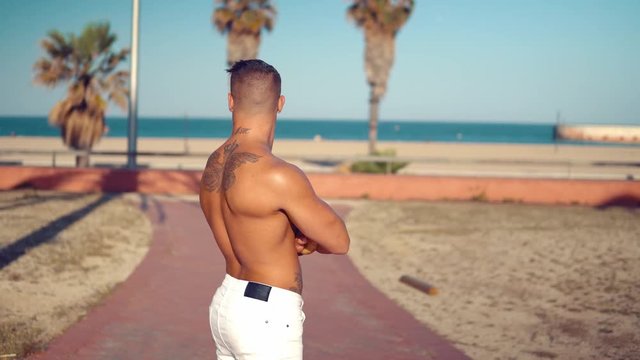Tattooed bodybuilder sexy male coach at the beach. He stands and shows his muscles