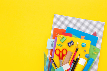 Back to school concept. Stack of notebooks and stationery on yellow background.